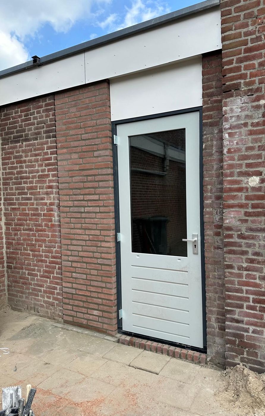 Nieuwe buitendeur met slot en hang-en-sluitwerk in een gemetselde gevel